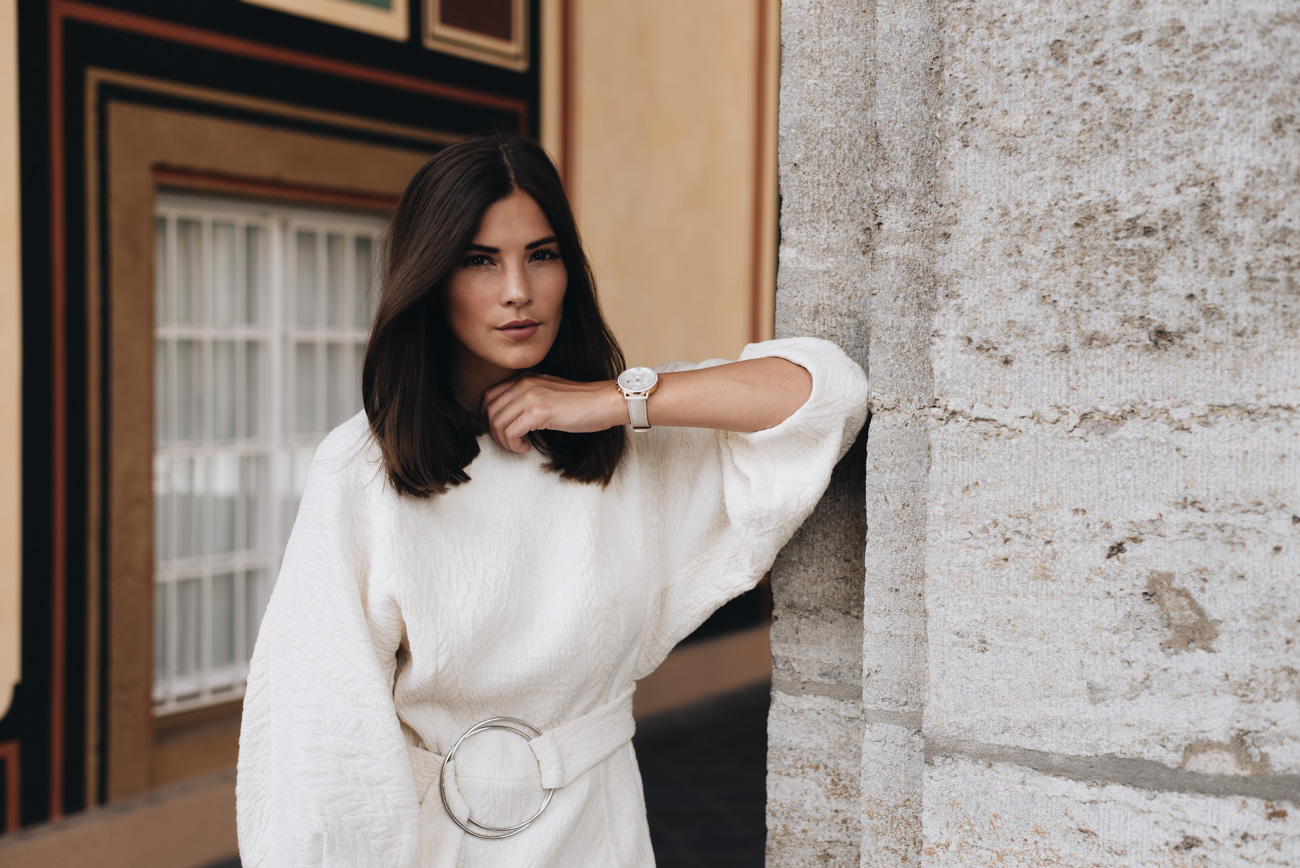 Woman in white sweater dress standing against wall.