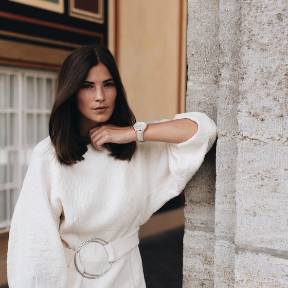 Woman in white sweater dress standing against wall.