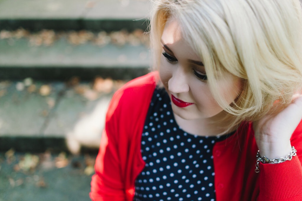 Blonde woman with red lipstick and red cardigan.